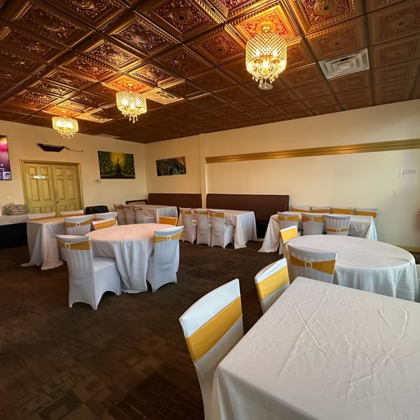 Empty dining room at Mayuri Indian Cuisine with tables draped in white and chairs with gold sashes.