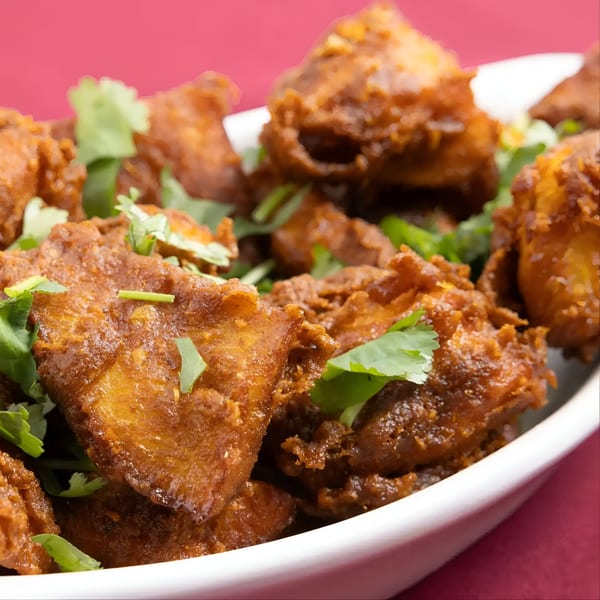 Close-up of golden-brown Indian chicken pakora or paneer pakora, garnished with fresh cilantro in a white bowl.