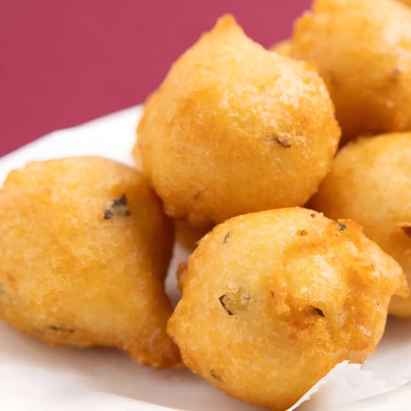 Close-up of golden-brown Indian fritters, possibly pakoras, on a white plate against a maroon background.