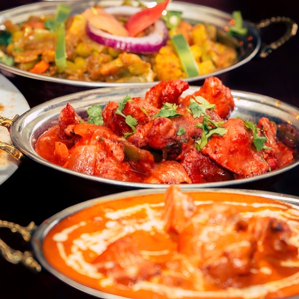 Three Indian dishes in metal bowls: chicken tikka, butter chicken, and a vegetable curry.