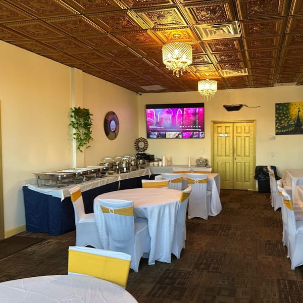 Mayuri Indian Cuisine's dining room with buffet tables, round tables with white and gold chairs, and a TV.
