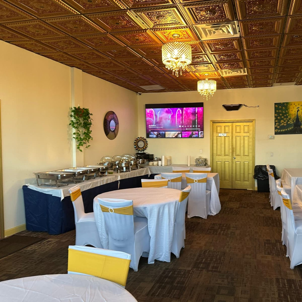Mayuri Indian Cuisine's dining room with buffet tables, round tables with white and gold chairs, and a TV.