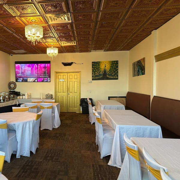 Mayuri Indian Cuisine dining room with white tablecloths, gold chair sashes, and a gold patterned ceiling.